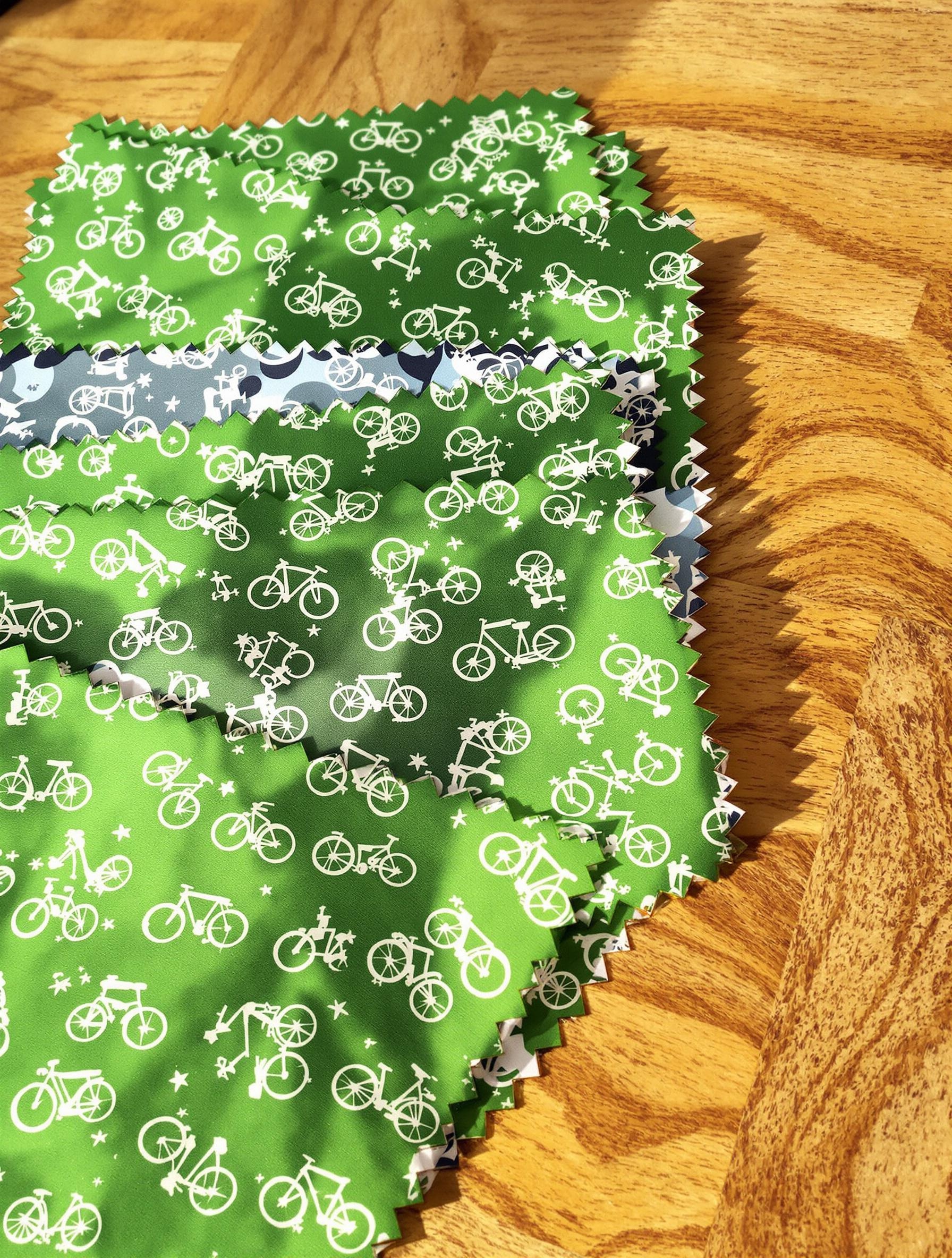 Coupons de tissu verts à motifs vélo imperméables, soigneusement disposés sur un plan de travail en bois.