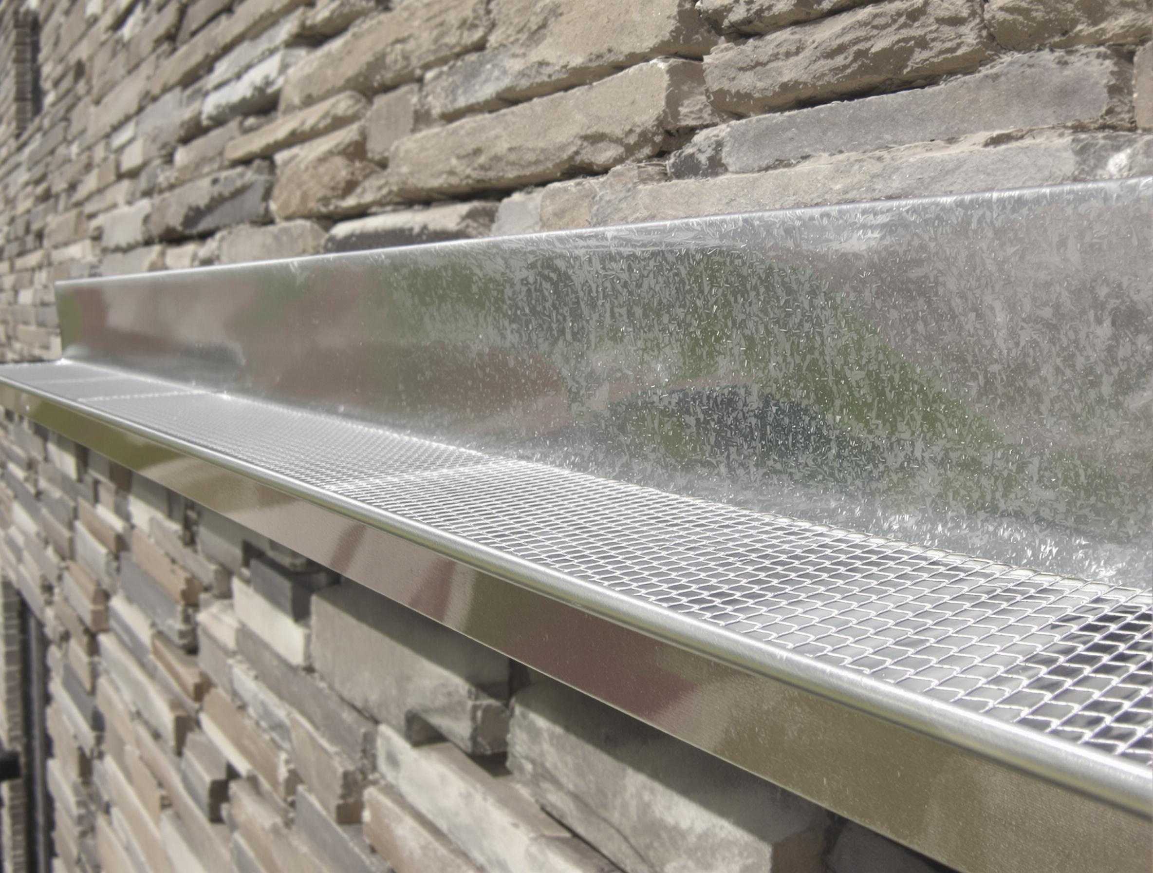 Gouttière en zinc posée contre une façade de schiste, détail pente, protection anti-feuilles.