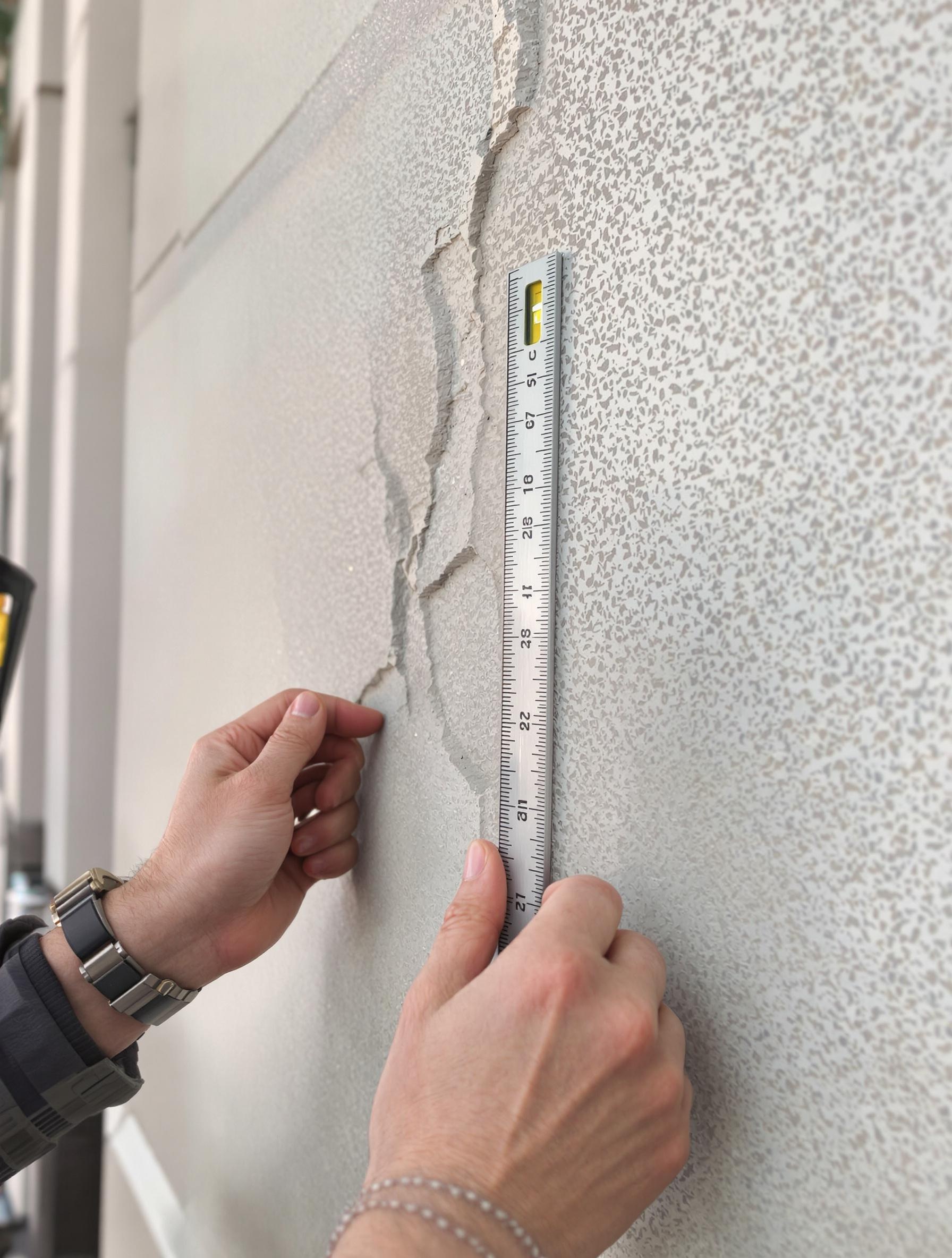 Mesure précise d’une microfissure de façade avec une réglette et un niveau à bulle