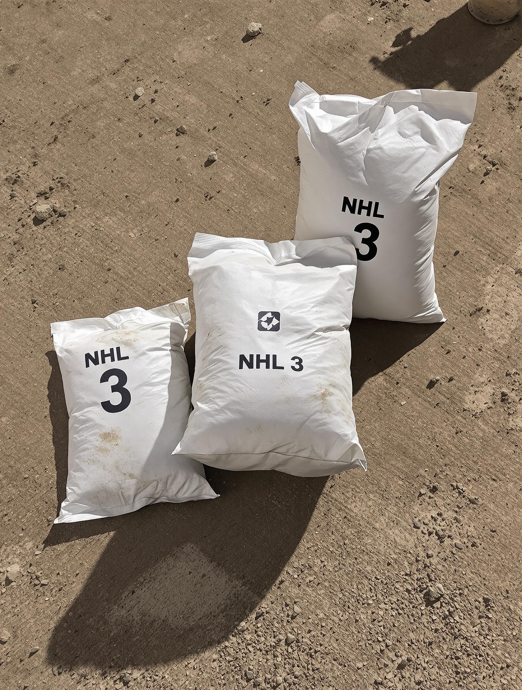 Sacs blancs marqués NHL 3 prêts à l’emploi, posés sur un sol de chantier poussiéreux
